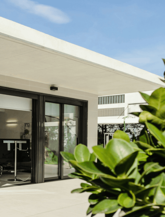 Pr3 Entrance to a modern building with glass doors, framed by green foliage