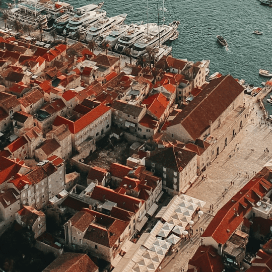 Aerial view of an old town with terracotta roofs and a waterfront promenade lined with yachts